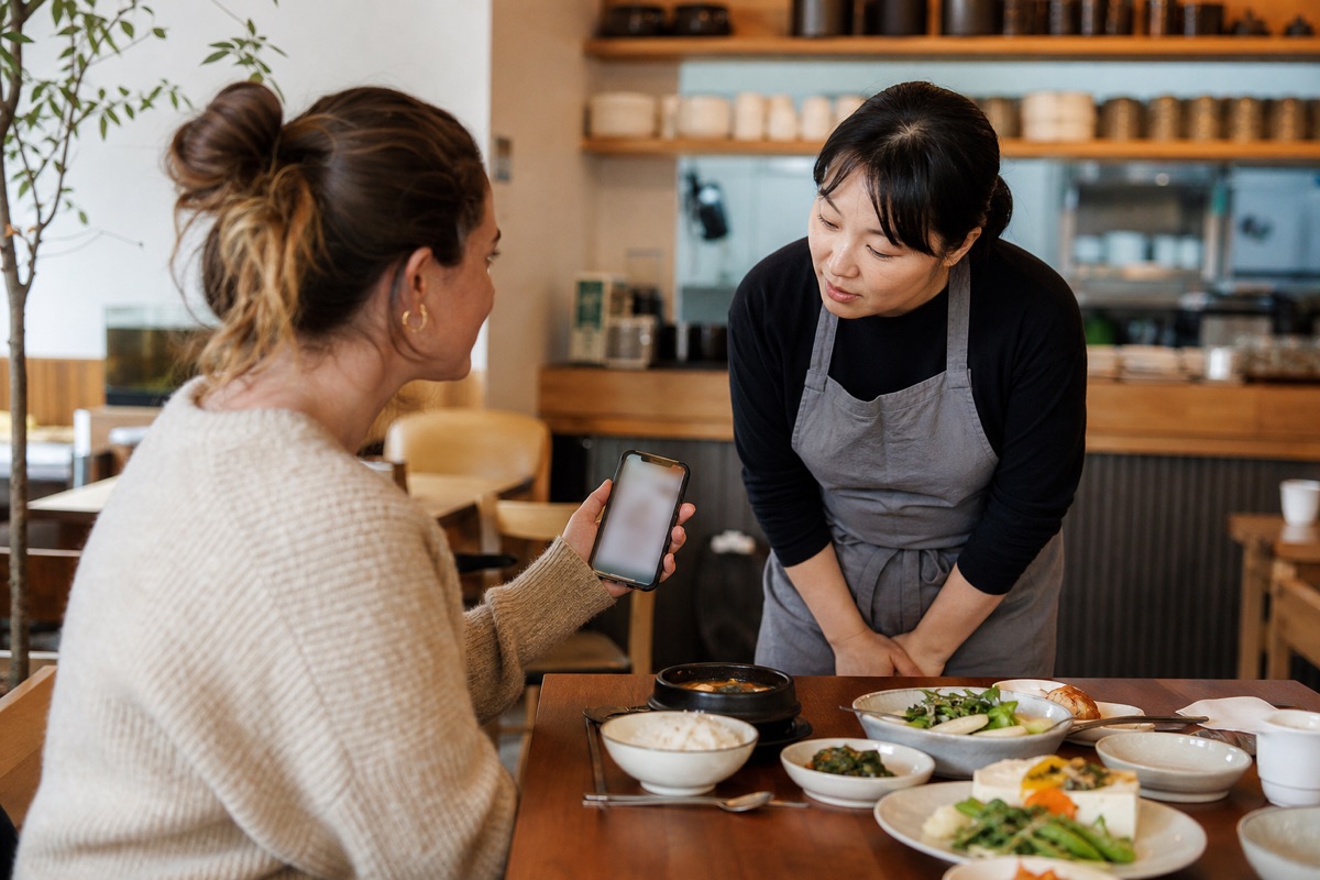 Diner showing an ingredient note on a phone to a Korean restaurant server