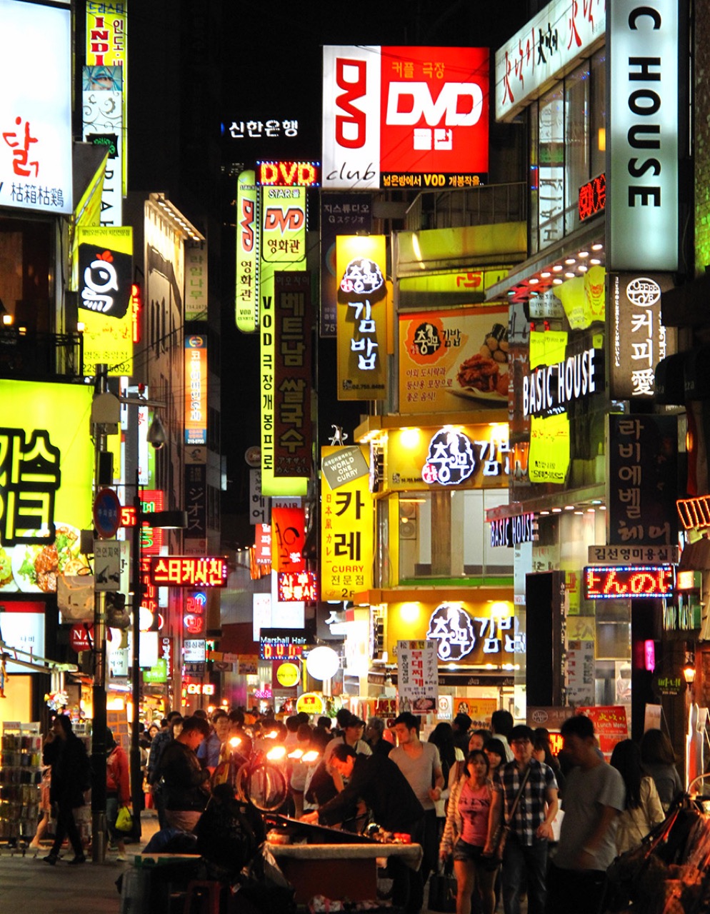 Vertical neon restaurant and shop signs glowing above a Myeongdong lane at night